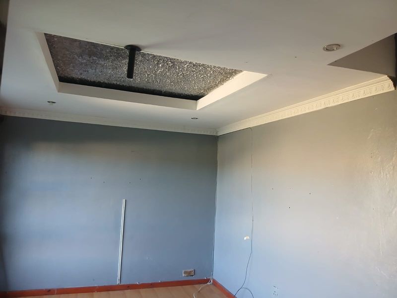 An empty bedroom featuring a recessed ceiling detail, decorative cornice, and laminate flooring, requiring minor cosmetic repairs and finishing touches.