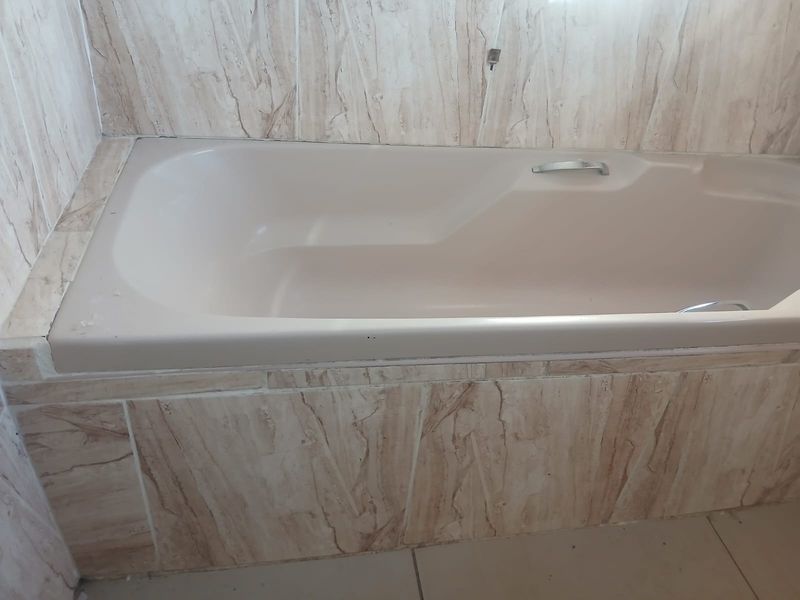 A bathroom featuring a built-in bathtub with neutral marble-effect wall tiling and floor tiles.
