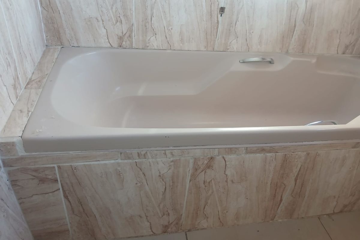A bathroom featuring a built-in bathtub with neutral marble-effect wall tiling and floor tiles.
