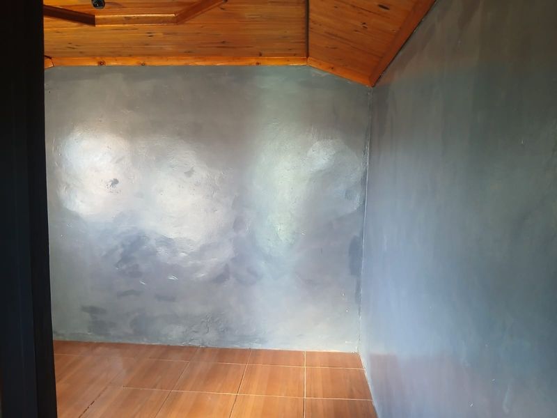 An empty bedroom featuring a timber ceiling and tiled flooring, with walls requiring refinishing or repainting.