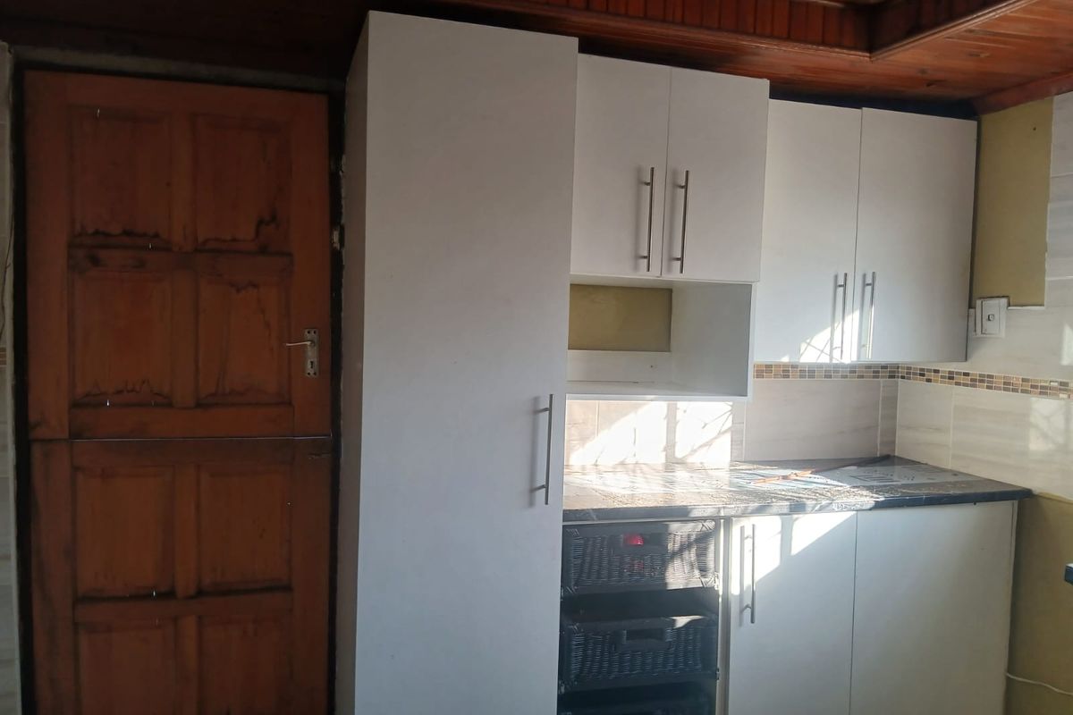 A compact kitchen area featuring white built-in cabinetry, a tiled backsplash, and a timber ceiling, requiring minor finishing and cosmetic updates.