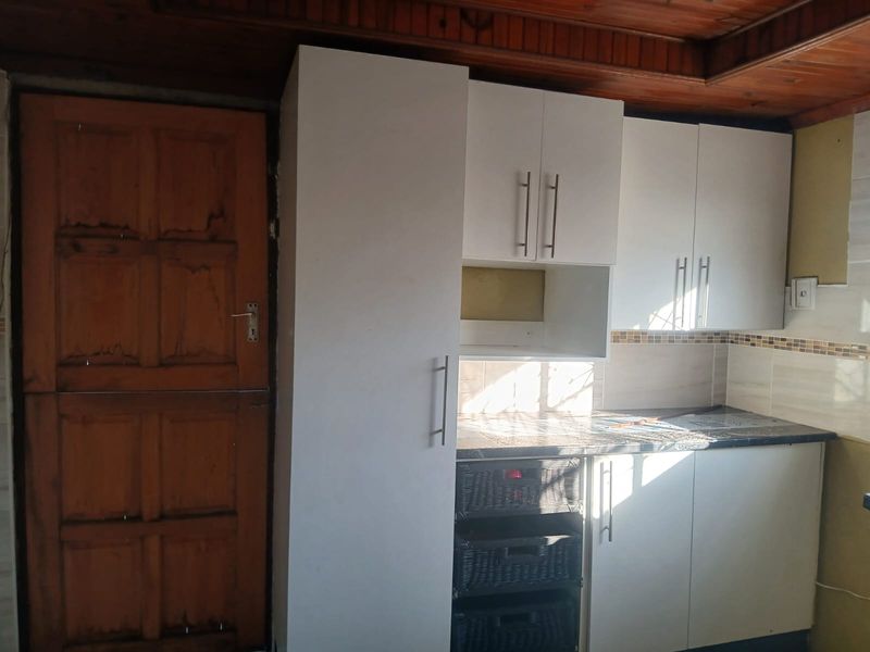 A compact kitchen area featuring white built-in cabinetry, a tiled backsplash, and a timber ceiling, requiring minor finishing and cosmetic updates.