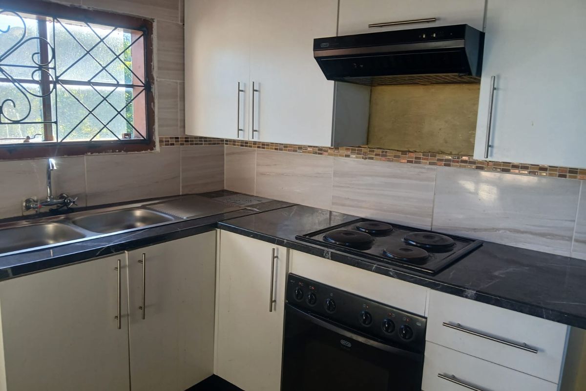 Functional kitchen featuring white cabinetry, dark countertops, built-in oven, electric hob, extractor fan, and a stainless steel double sink with tiled backsplash.