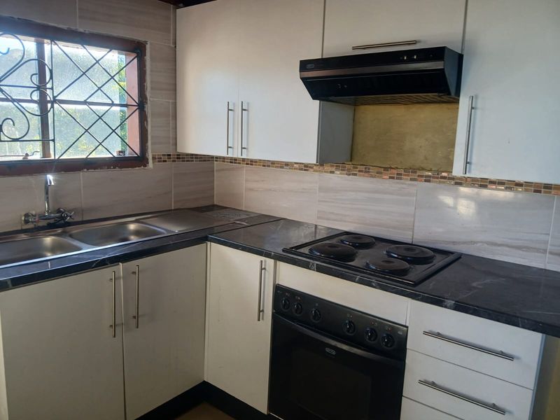 Functional kitchen featuring white cabinetry, dark countertops, built-in oven, electric hob, extractor fan, and a stainless steel double sink with tiled backsplash.