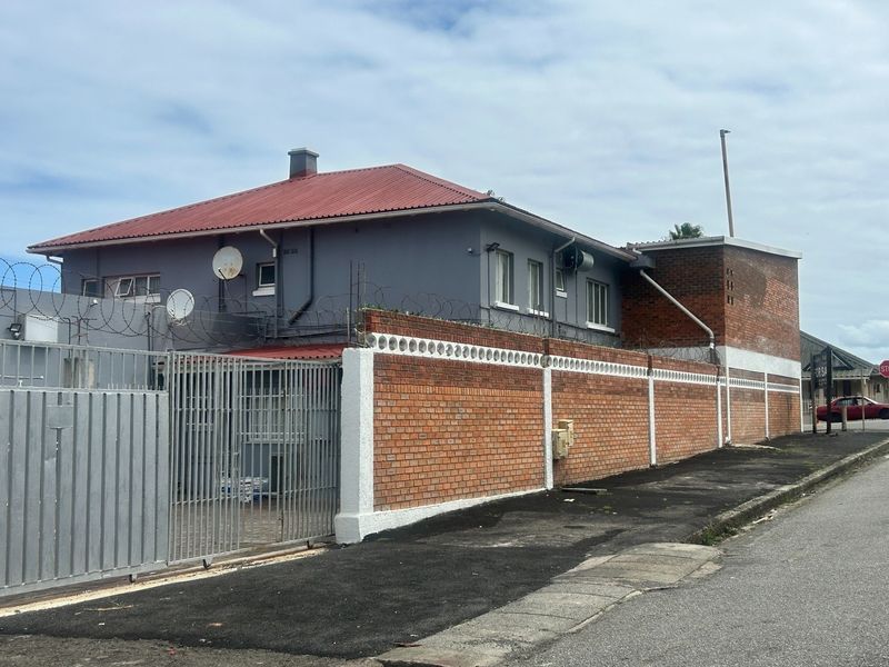 Exterior view of a property featuring a red metal roof, brick perimeter wall with security razor wire, and a metal sliding gate.