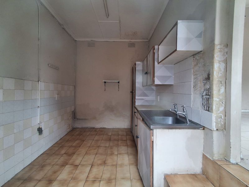 A dated, empty kitchen space featuring tiled flooring, a stainless steel sink, and built-in cabinetry, requiring significant renovation and cosmetic updates.
