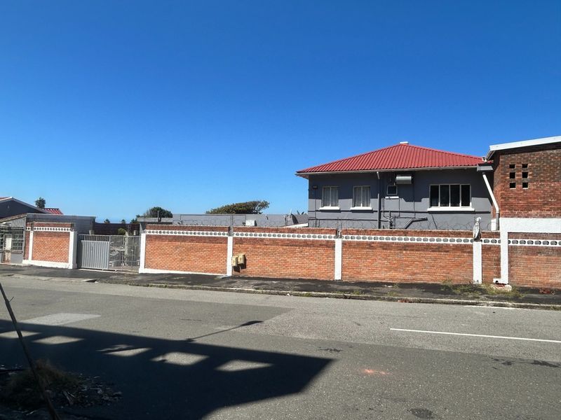 Street view of the property showing the brick boundary wall with security razor wire and the exterior facade of the house with a red roof.