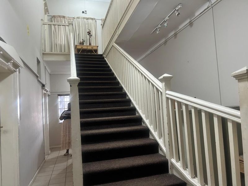 A central hallway featuring a prominent staircase with a wooden balustrade, tiled flooring, and overhead track lighting.