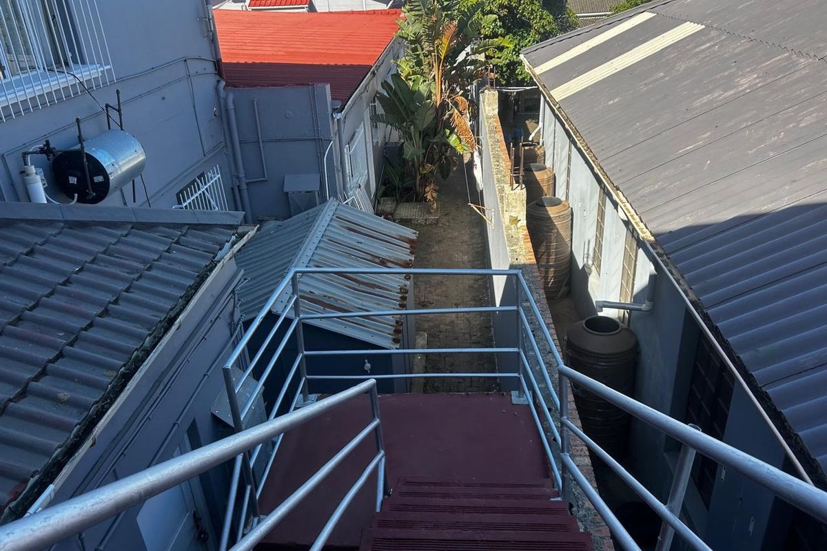 An elevated view of the rear exterior area featuring a metal staircase, water storage tanks, and surrounding building structures.