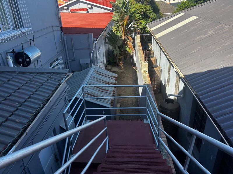 An elevated view of the rear exterior area featuring a metal staircase, water storage tanks, and surrounding building structures.