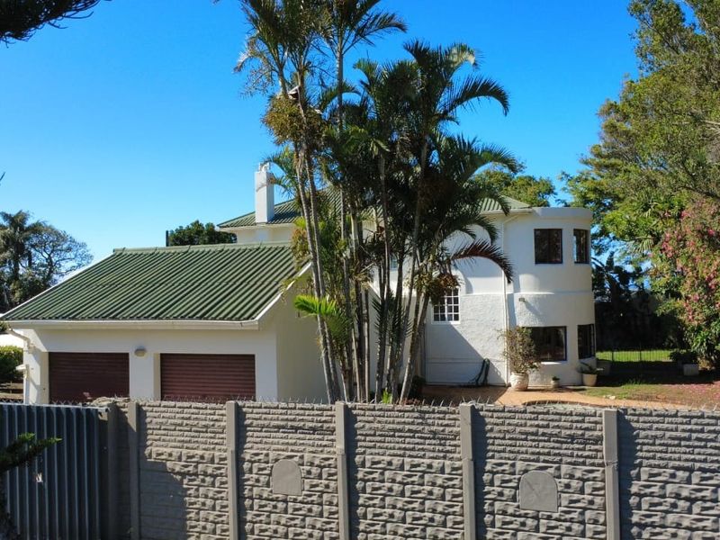 Front view of a two-story house featuring a double garage, green metal roof, and a secure precast concrete boundary wall with security spikes.