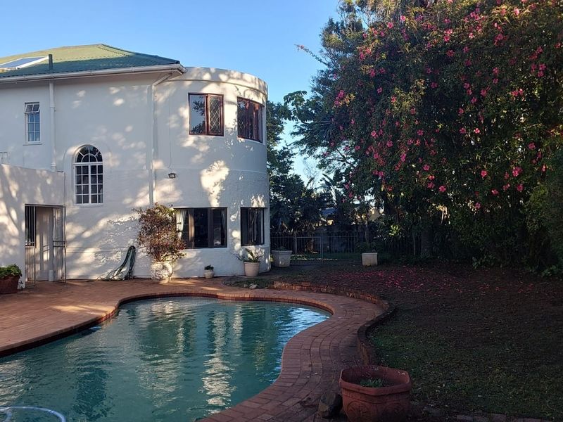 Rear exterior view featuring a swimming pool with brick coping, timber decking, and a distinctive curved building facade with leaded glass windows.