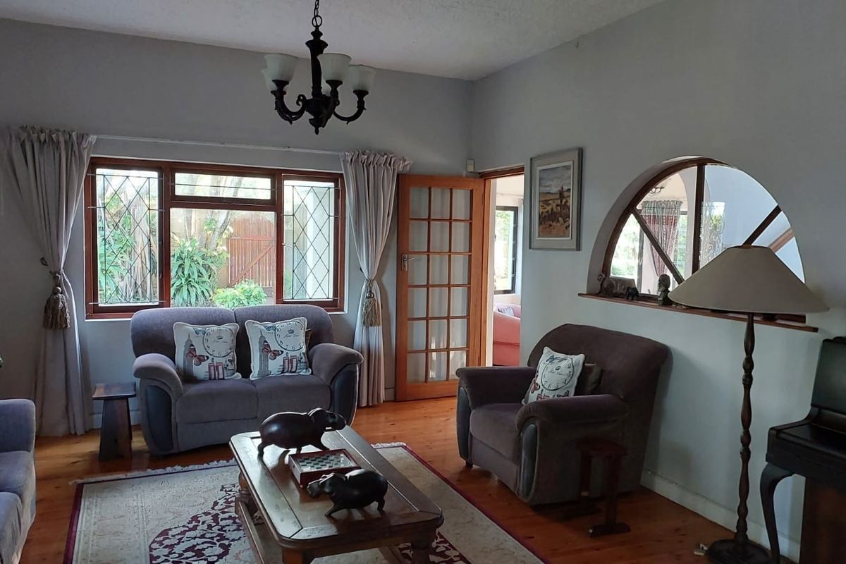 A cozy living room featuring warm hardwood flooring, classic leaded glass windows, and a distinctive arched interior window opening to an adjacent space.