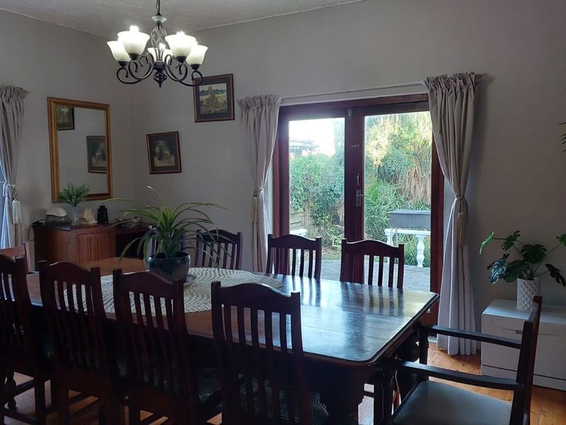 A dining room featuring warm wooden flooring, a classic chandelier, and double french doors providing direct access to the rear garden.