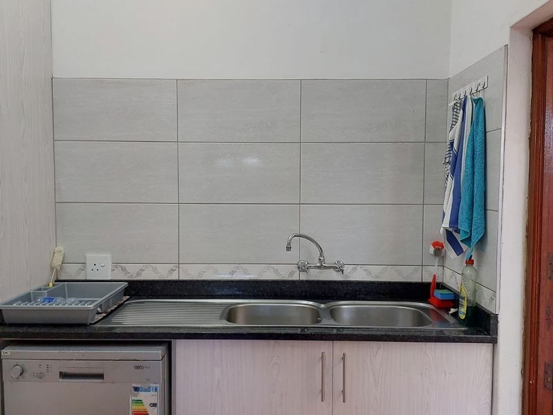 A functional scullery area featuring a double bowl stainless steel sink, granite countertops, and tiled splashback with built-in cabinetry.