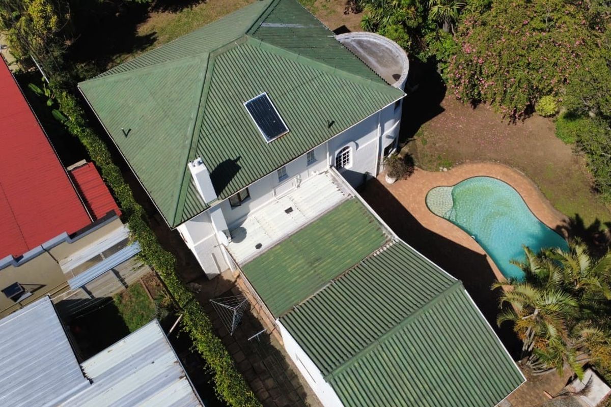 Aerial view of the property showing the green corrugated metal roof, solar water heater, chimney, and an outdoor swimming pool with surrounding garden area.