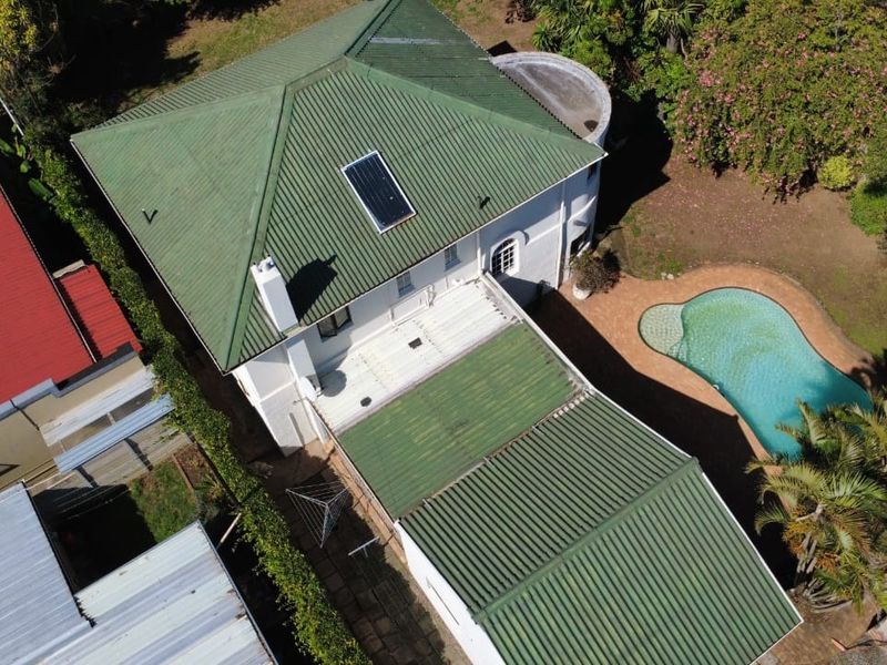 Aerial view of the property showing the green corrugated metal roof, solar water heater, chimney, and an outdoor swimming pool with surrounding garden area.
