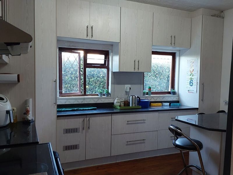 A functional kitchen featuring light wood-grain cabinetry, dark granite countertops, an integrated extractor fan, and a breakfast nook with timber flooring.