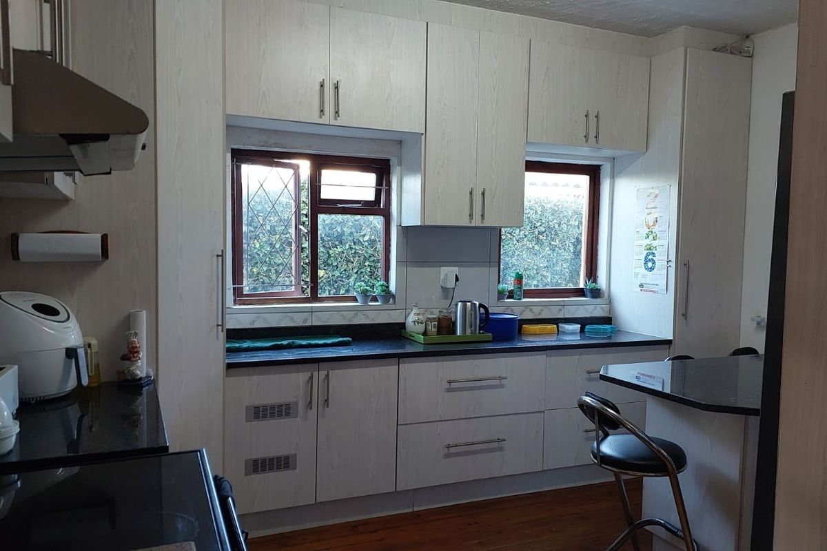 A functional kitchen featuring light wood-grain cabinetry, dark granite countertops, an integrated extractor fan, and a breakfast nook with timber flooring.