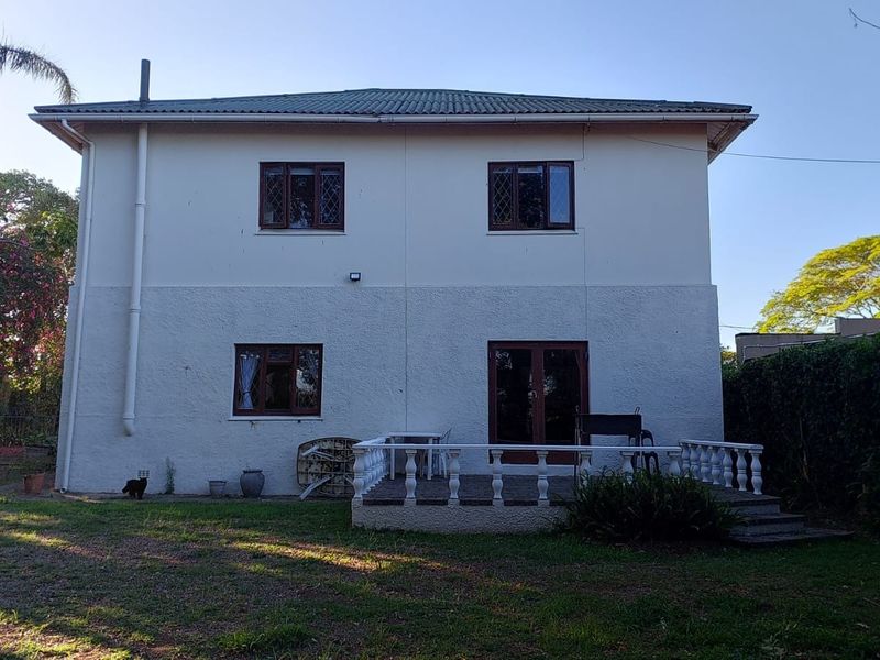 Rear view of a two-story house featuring a concrete patio with balustrades, leaded glass windows, and a spacious garden area.