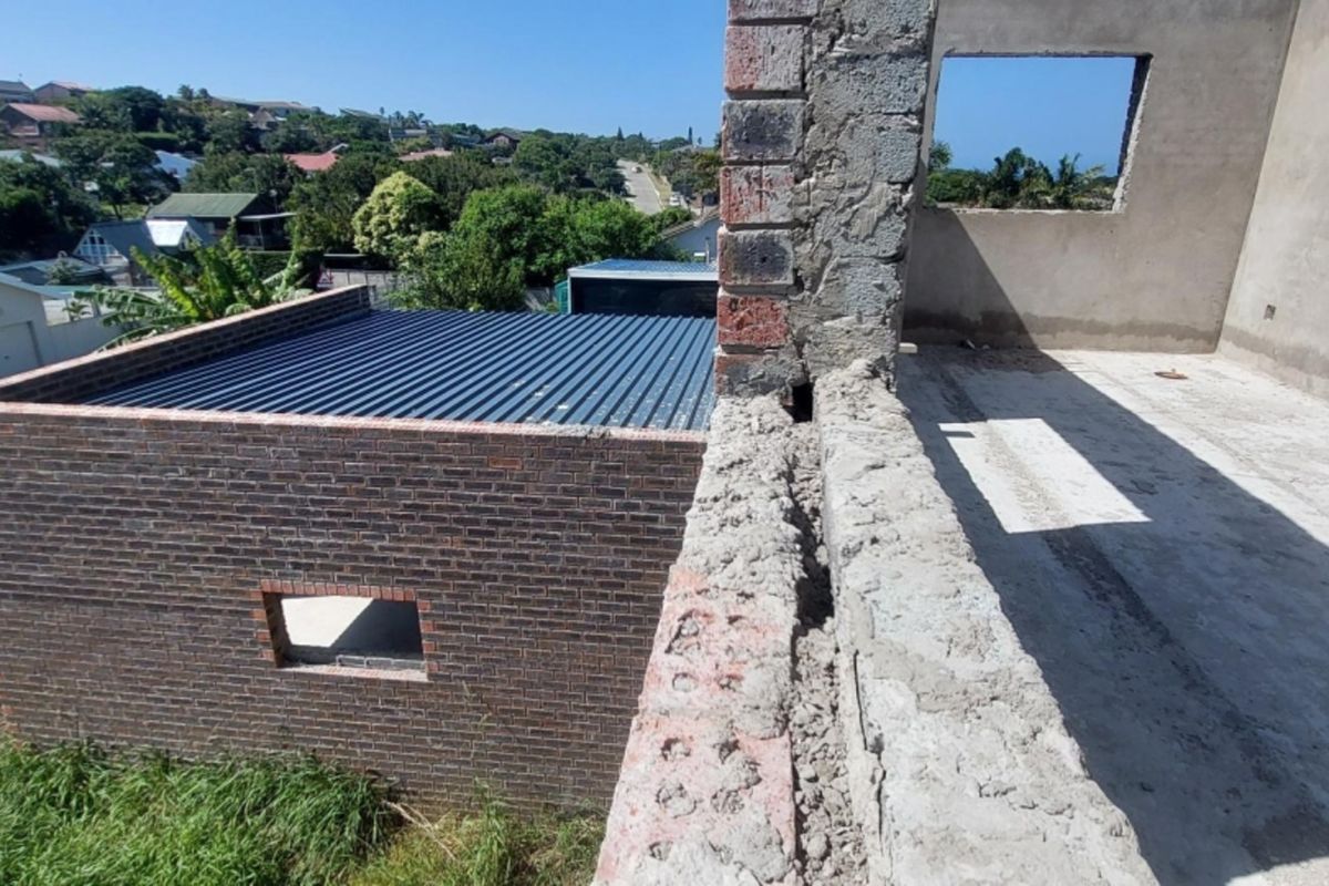 An elevated view of a property under construction, featuring exposed brickwork, a corrugated metal roof, and unfinished concrete structural elements.