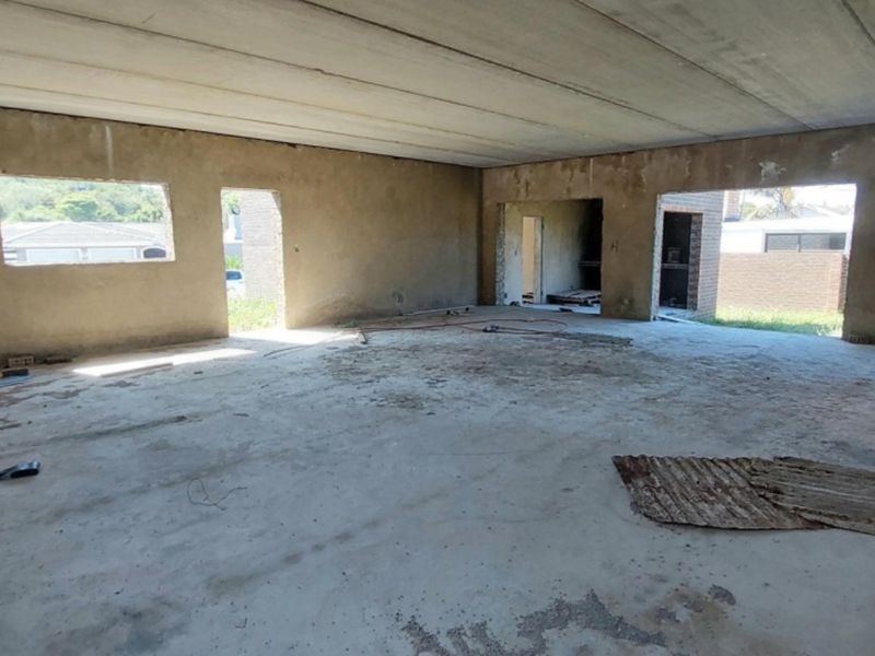 A large, open-plan interior space currently in a shell state with unfinished concrete floors, exposed ceiling panels, and plastered brick walls.