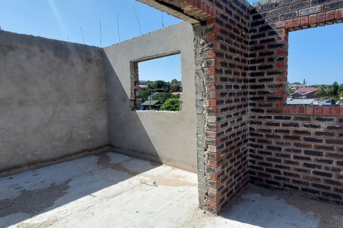 An unfinished room under construction featuring exposed brick walls, cement flooring, and open window frames, offering a blank canvas for completion.