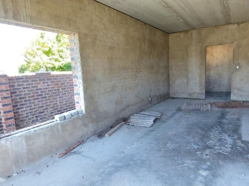An unfinished interior space in shell condition, featuring raw plastered walls, concrete flooring, and a large window opening, ready for final finishes.