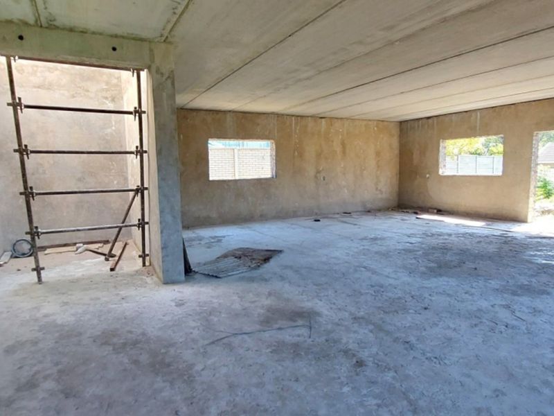 An expansive, unfinished open-plan interior space featuring raw concrete walls, flooring, and ceiling, currently in a shell construction state.