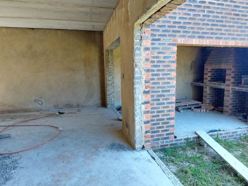 An unfinished outdoor patio area featuring exposed brickwork, a built-in braai, and concrete flooring, currently in the construction phase.