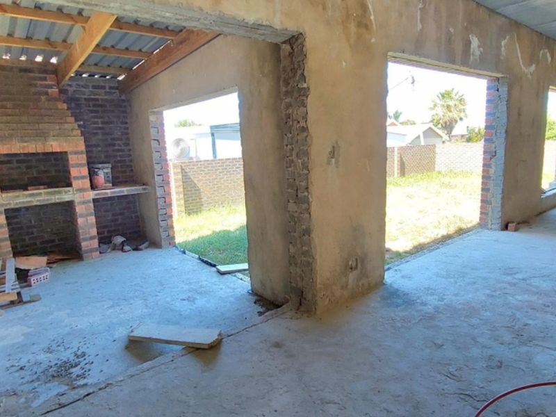 An unfinished covered patio area featuring a built-in brick braai, exposed brick walls, and concrete flooring, currently in a shell construction state.