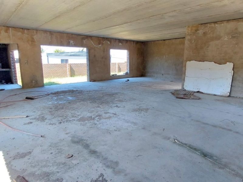 An expansive, unfinished open-plan living area featuring raw concrete flooring, exposed ceiling, and a built-in brick fireplace, offering a blank canvas for renovation.