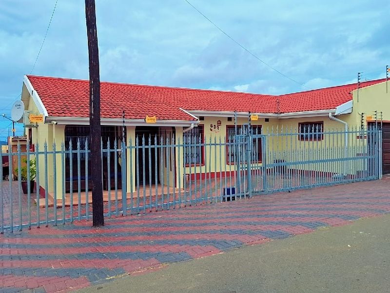 Front elevation of a single-story house featuring a red tiled roof, paved driveway, and secure perimeter fencing with an integrated gate.