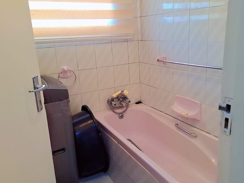 A compact bathroom featuring a built-in bathtub, wall tiling, and a functional mixer tap, offering potential for a modern renovation.