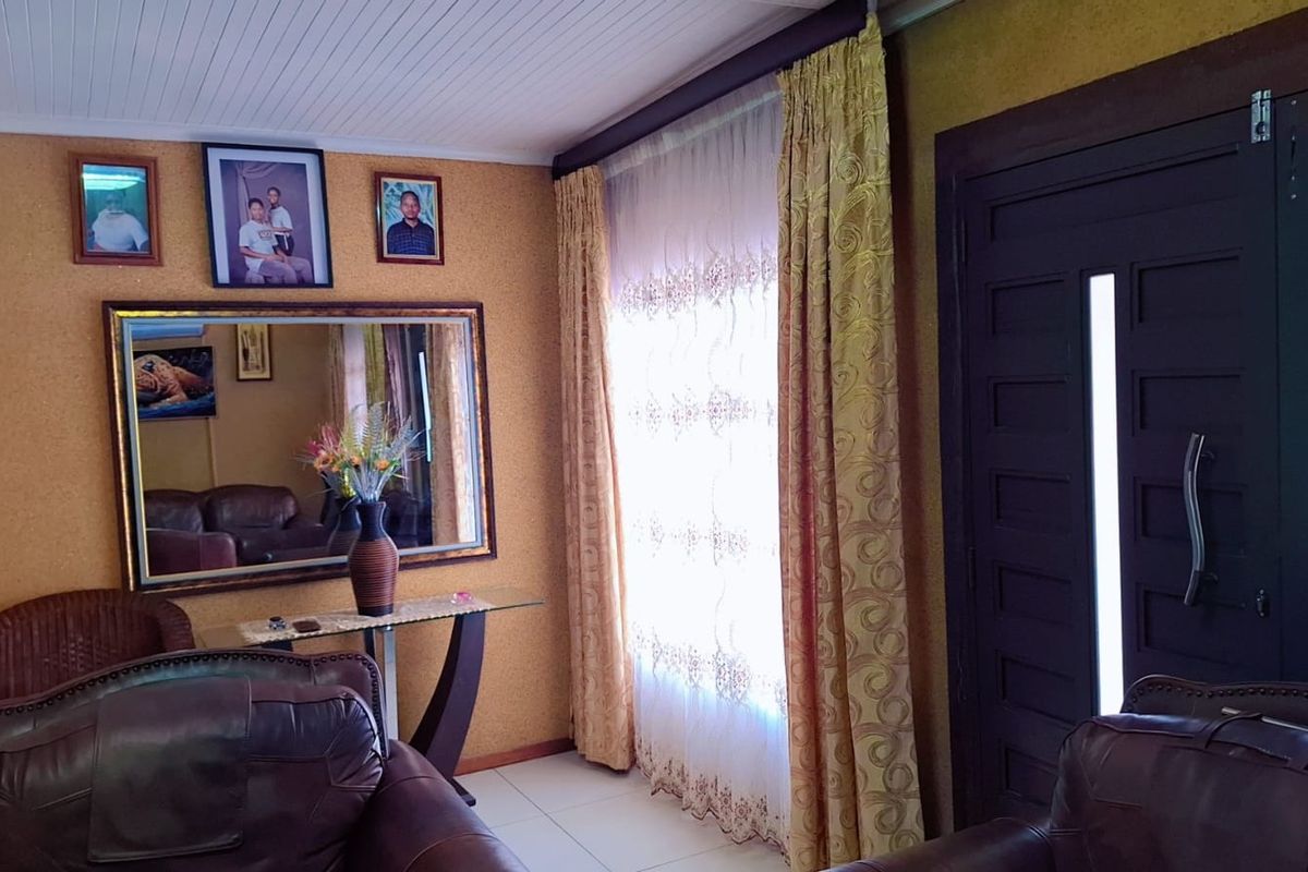 A living room featuring tiled flooring, a timber panelled ceiling, and a solid panelled entrance door with natural light filtering through window curtains.