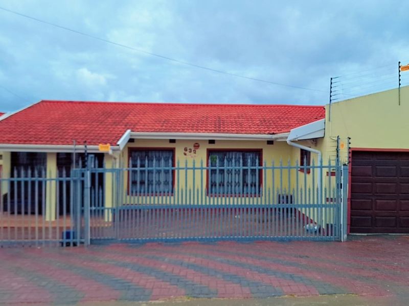 Front elevation of a single-story house featuring a red tiled roof, paved driveway, secure metal fencing, and an integrated garage.