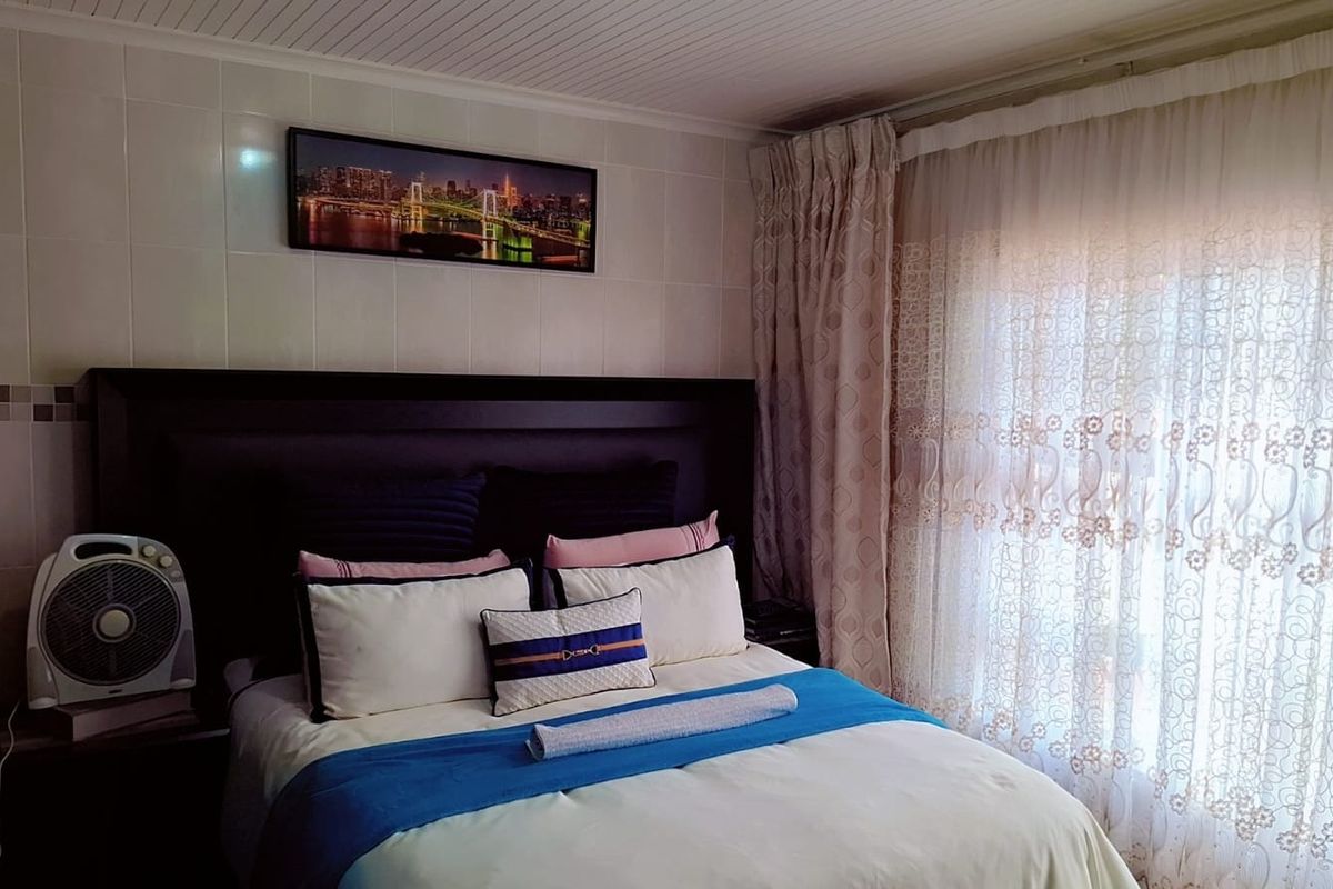 A bedroom featuring tiled wall finishes and a tongue and groove ceiling, providing a functional space with natural light through window curtains.