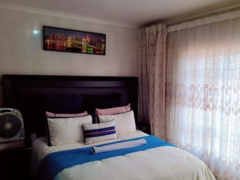 A bedroom featuring tiled wall finishes and a tongue and groove ceiling, providing a functional space with natural light through window curtains.