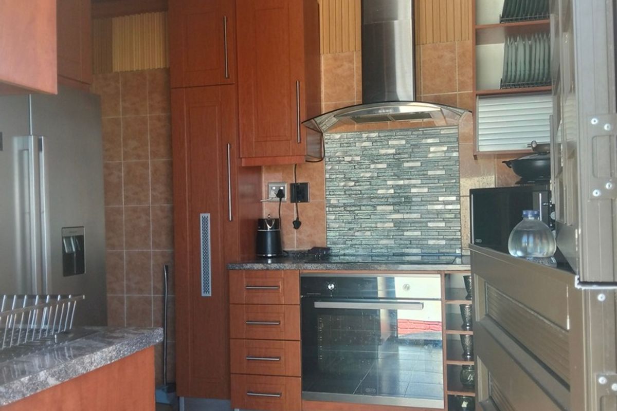 A functional kitchen featuring wood-toned cabinetry, stone countertops, a tiled backsplash, and a stainless steel extractor fan with a timber-paneled ceiling.