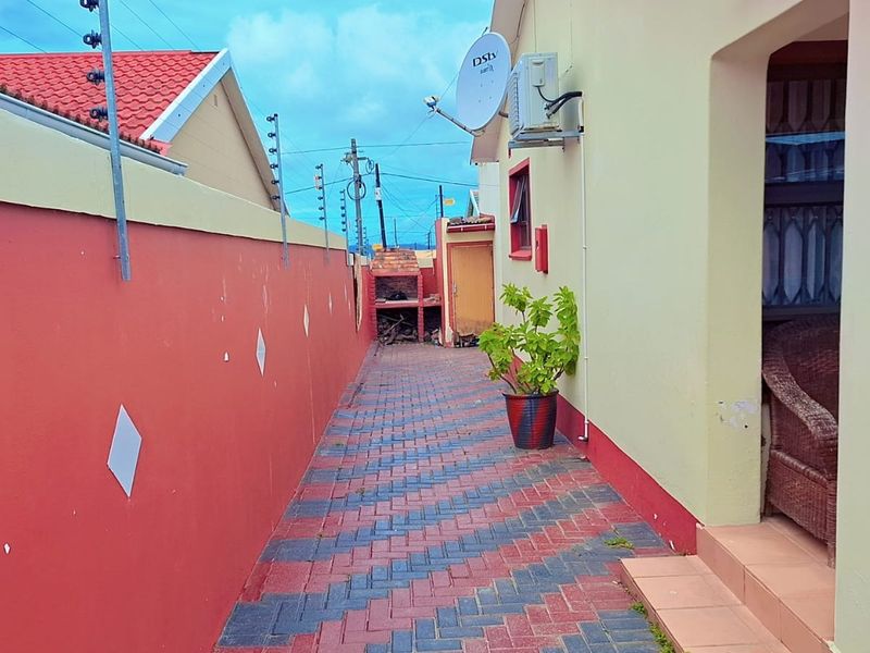 A paved side walkway featuring a built-in braai area, enclosed by a boundary wall with electric fencing and an external air conditioning unit.