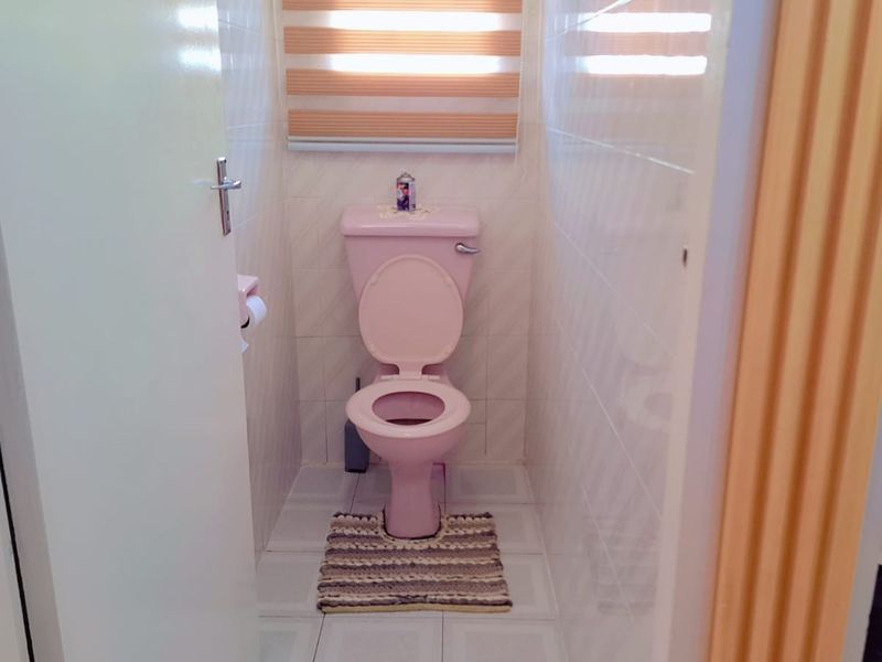 A compact bathroom featuring a classic pink toilet suite and fully tiled walls, with a glimpse of an adjacent bathtub area.