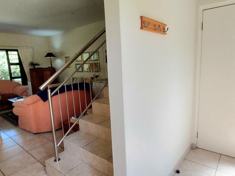 Entrance area featuring tiled flooring and a stainless steel staircase railing, leading into an open-plan living space.