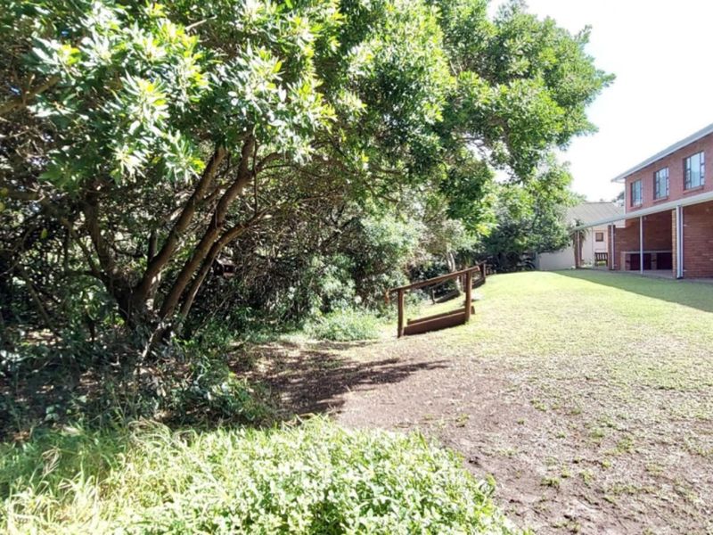 A view of the rear exterior of the townhouse, featuring a brick facade, a covered patio area, and a spacious lawn with mature trees.