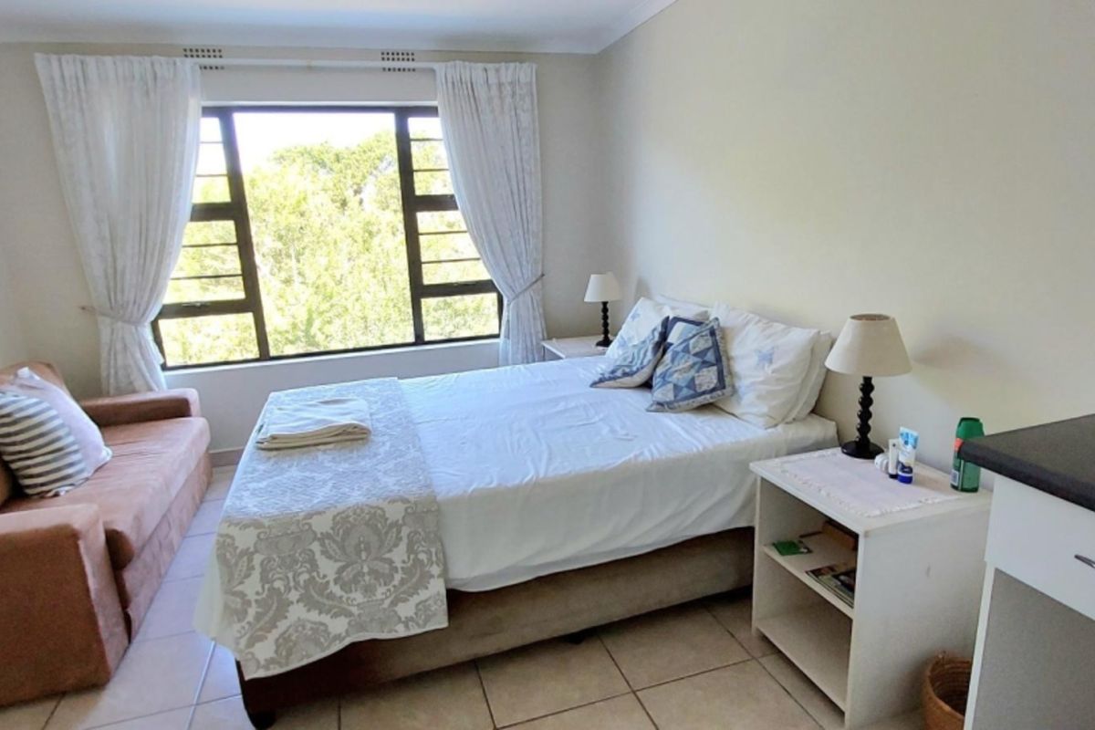 A functional bedroom featuring tiled flooring, large aluminium-framed windows providing natural light, and built-in cabinetry.
