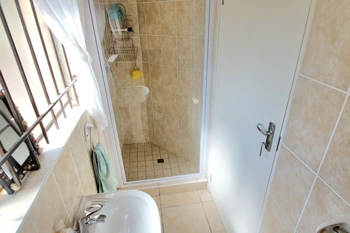 A compact bathroom featuring a tiled shower enclosure, pedestal basin, and tiled flooring with security bars on the window.