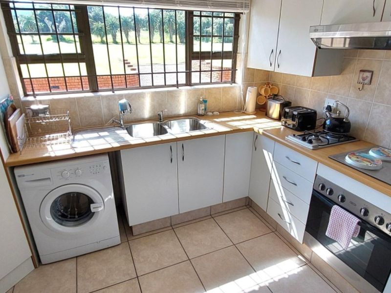A functional kitchen featuring white cabinetry, a built-in oven with gas hob, tiled splashbacks, and a window with security bars overlooking the exterior.