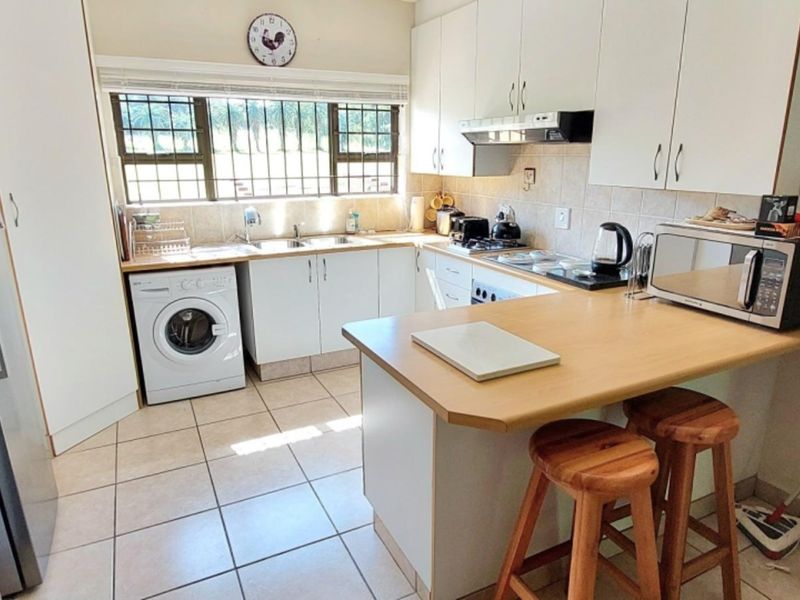 Functional kitchen featuring white cabinetry, laminate countertops, tiled flooring, and a breakfast nook, with integrated laundry plumbing and security bars on the window.