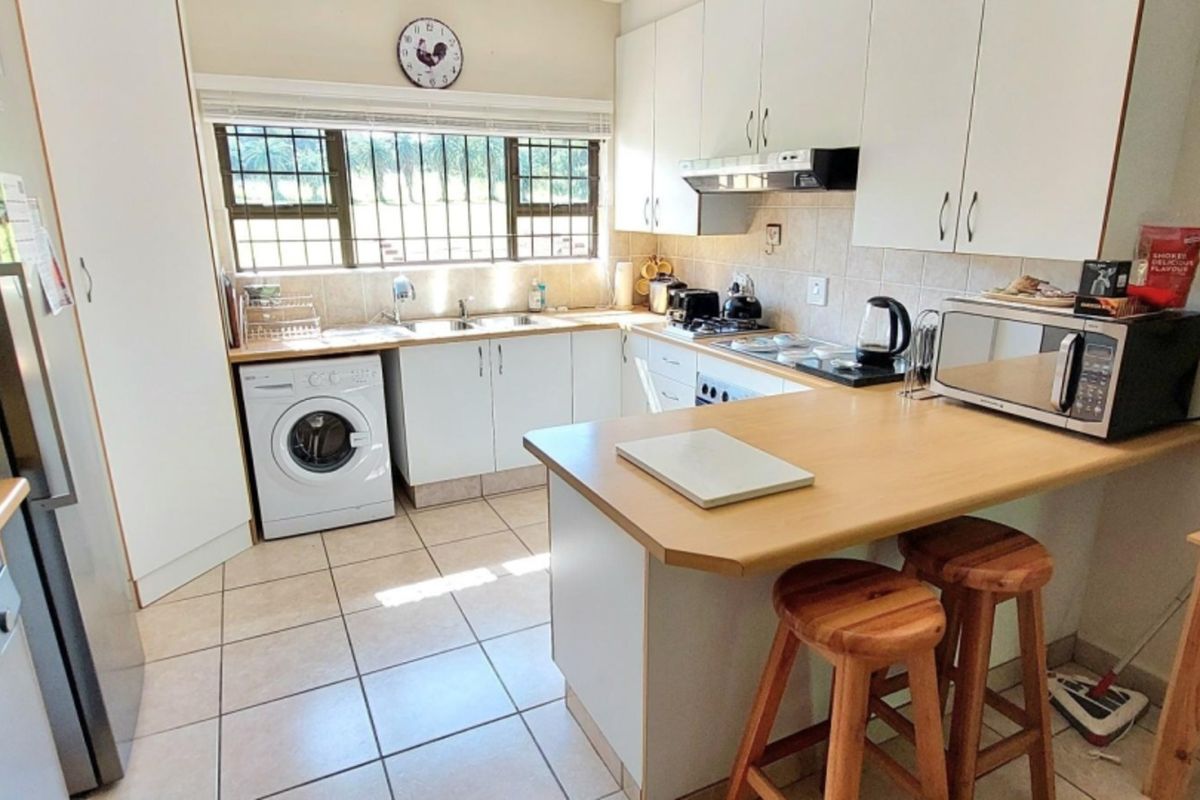 Functional kitchen featuring white cabinetry, laminate countertops, tiled flooring, and a breakfast nook, with integrated laundry plumbing and security bars on the window.