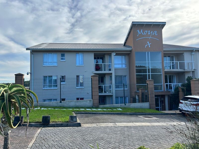 Front elevation of the Moya A apartment complex, featuring a modern facade with balconies, large glass windows, and paved driveway access.
