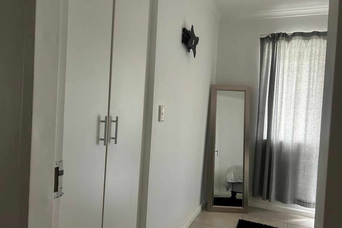 A bedroom featuring tiled flooring, a built-in wardrobe, and a wall-mounted TV bracket, offering a functional and neutral living space.